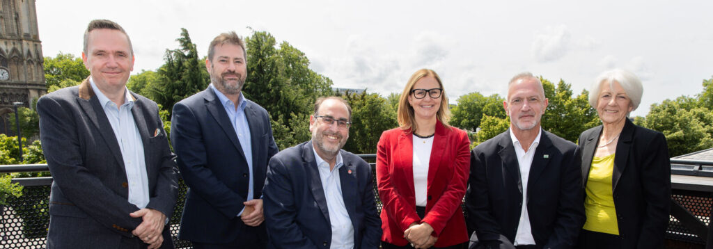 Senior leadership team of the West of England Mayoral Combined Authority standing together outdoors, with trees and a church tower visible in the background.