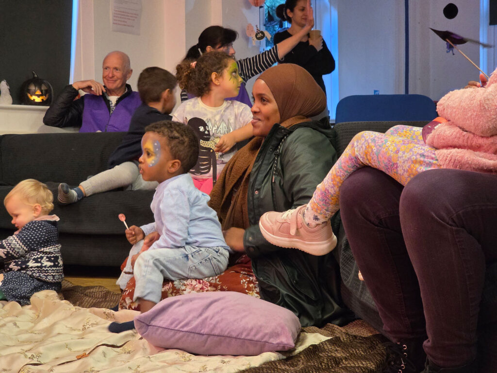 Families and children take part in a Bristol Charities community event, sitting together indoors during a relaxed, inclusive activity session.