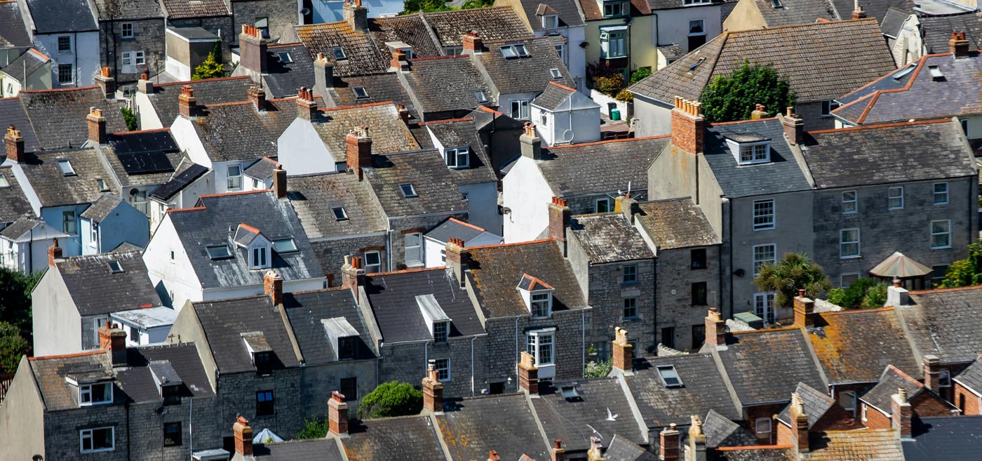 terraced-housig-roofs A dense cluster of terraced houses with gray slate roofs, varying in height and roof styles.