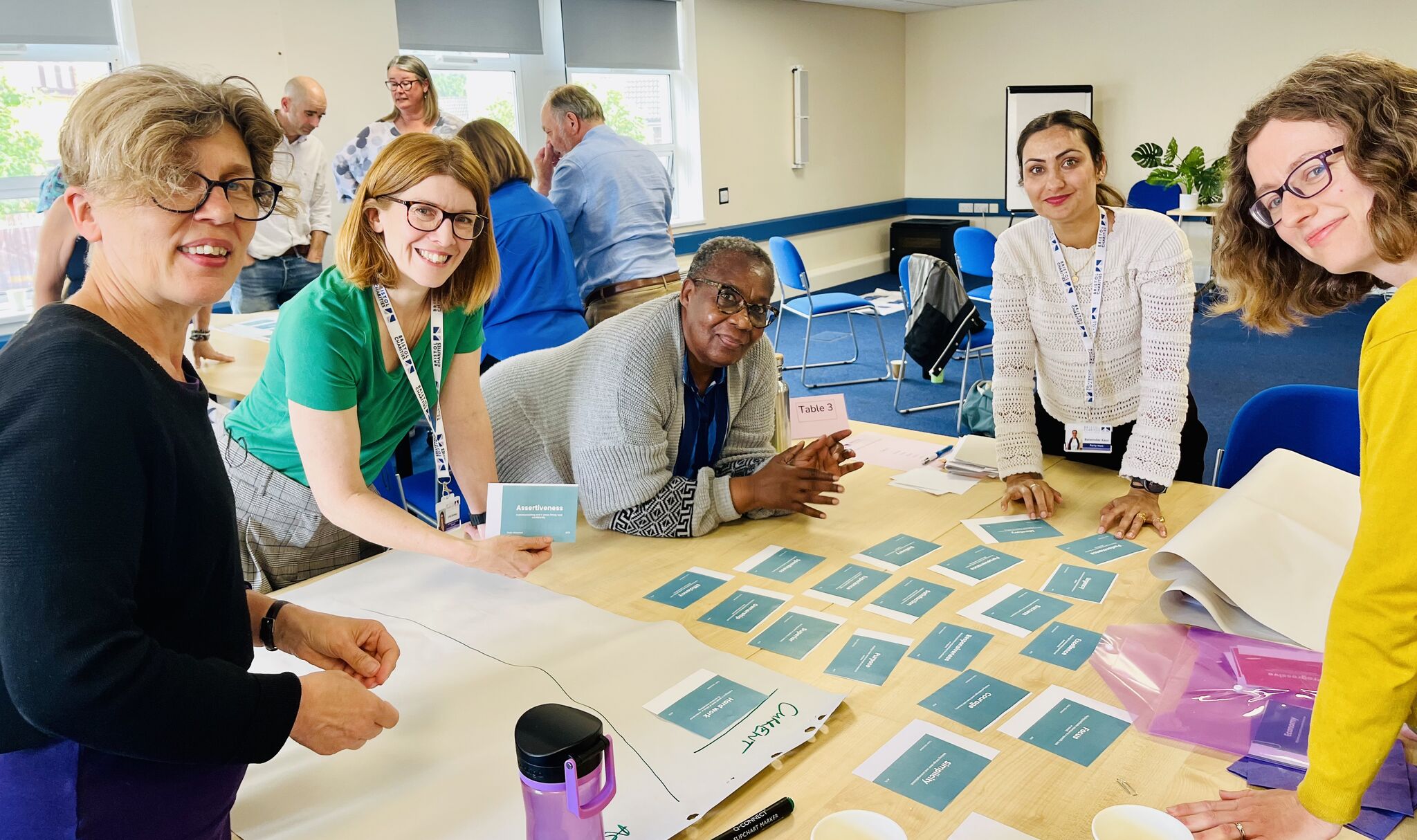 team with eileen and diana june 2026 A group of people are gathered around a table with teal sticky notes, working together.